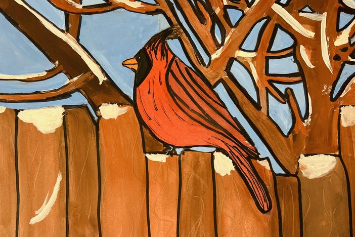 Red and black bird sits on a snow covered fence with branches of a snow covered tree in the background